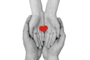 Familie, die kleines rotes Herz in den Händen hält, als Symbol der Fürsorge, Liebe und Gesundheitsversorgung. 