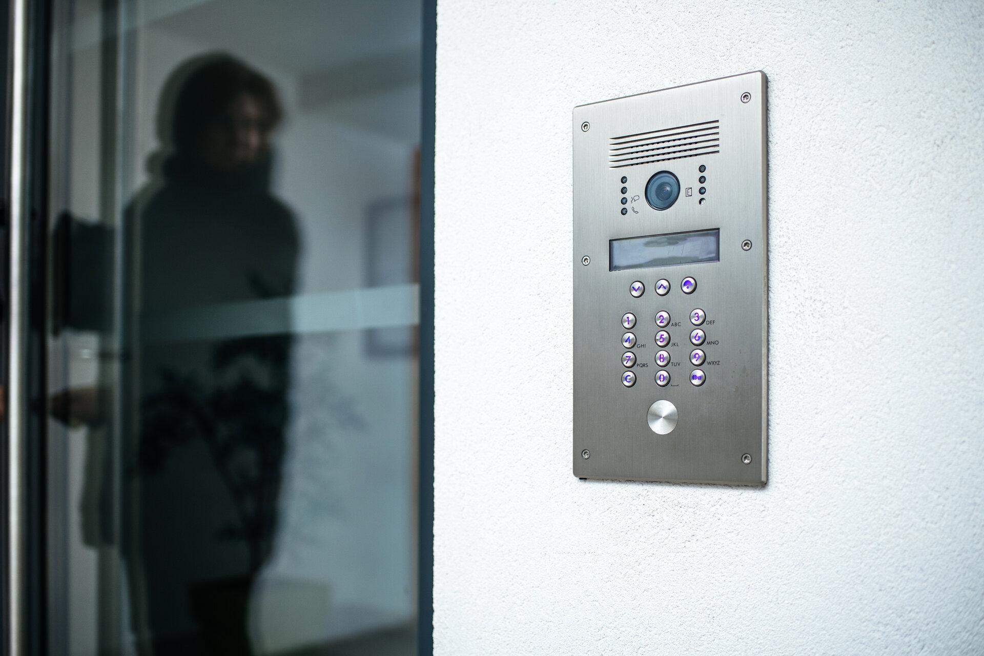 Frauensilhouette, die sich darauf vorbereitet, in ein modernes Haus einzutreten, mit Fokus auf der digitalen Türsprechanlage.