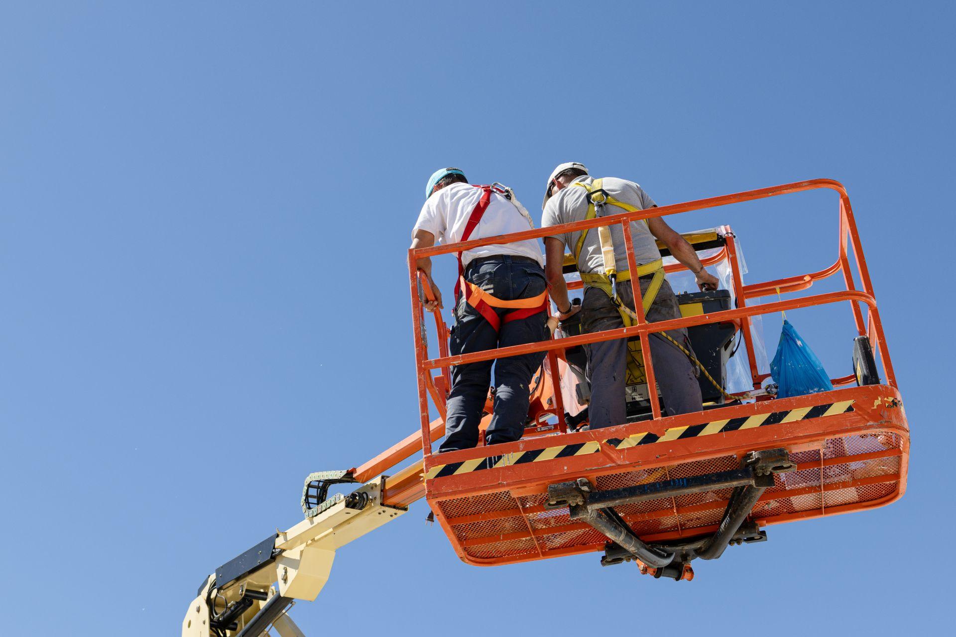 Zwei Arbeiter mit Sicherheitsausrüstung auf Arbeitsbühne bei blauem Himmel
