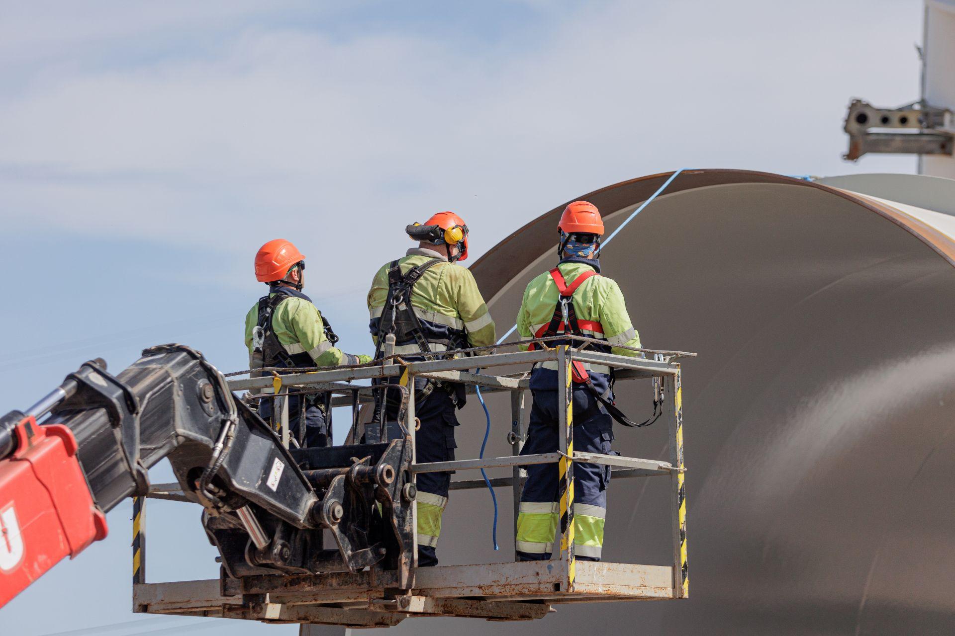 Drei Arbeiter auf Hubarbeitsbühne vor großer Metallstruktur